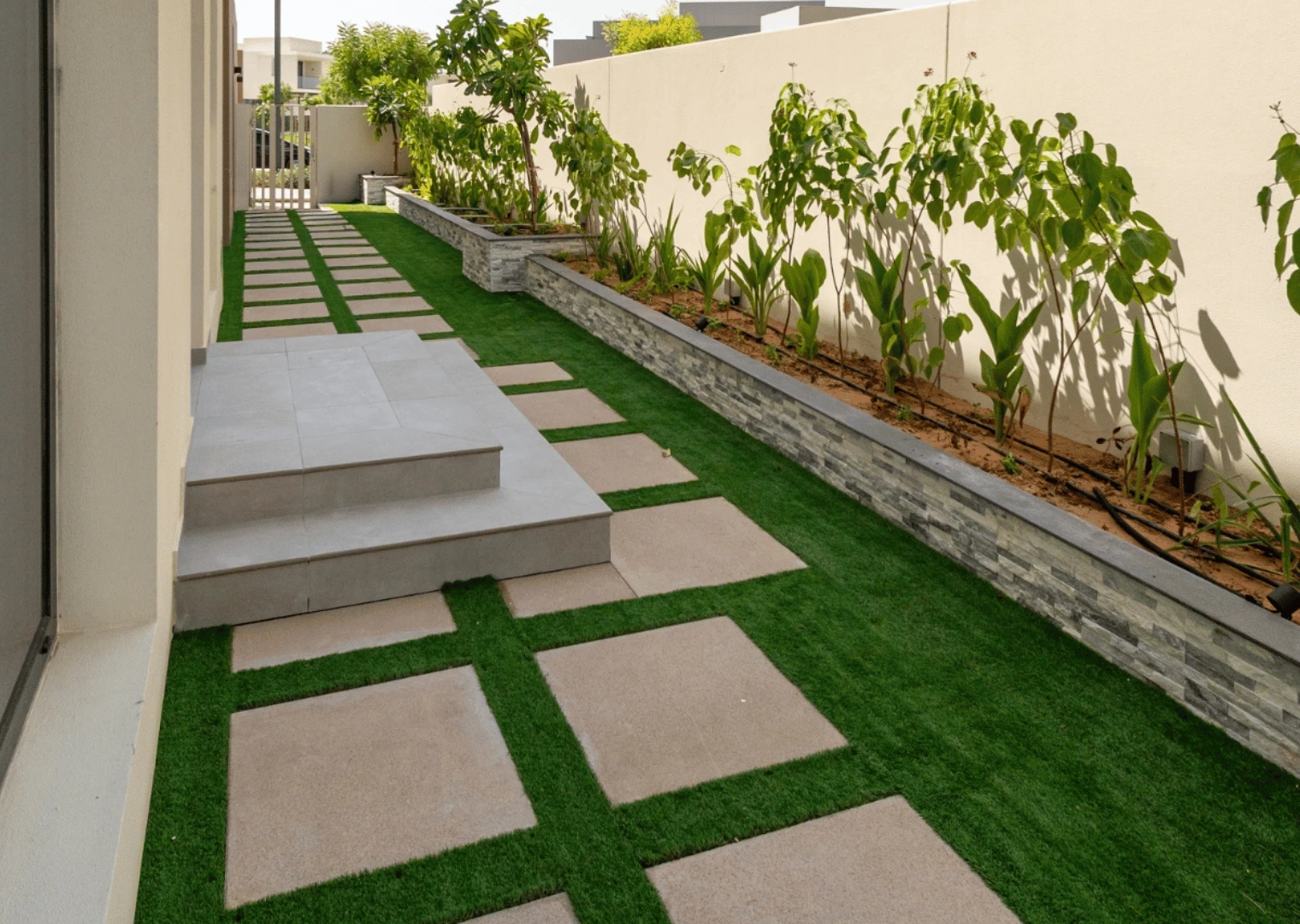 Side garden with raised stone-clad planter, plants and stepping stones in Dubai